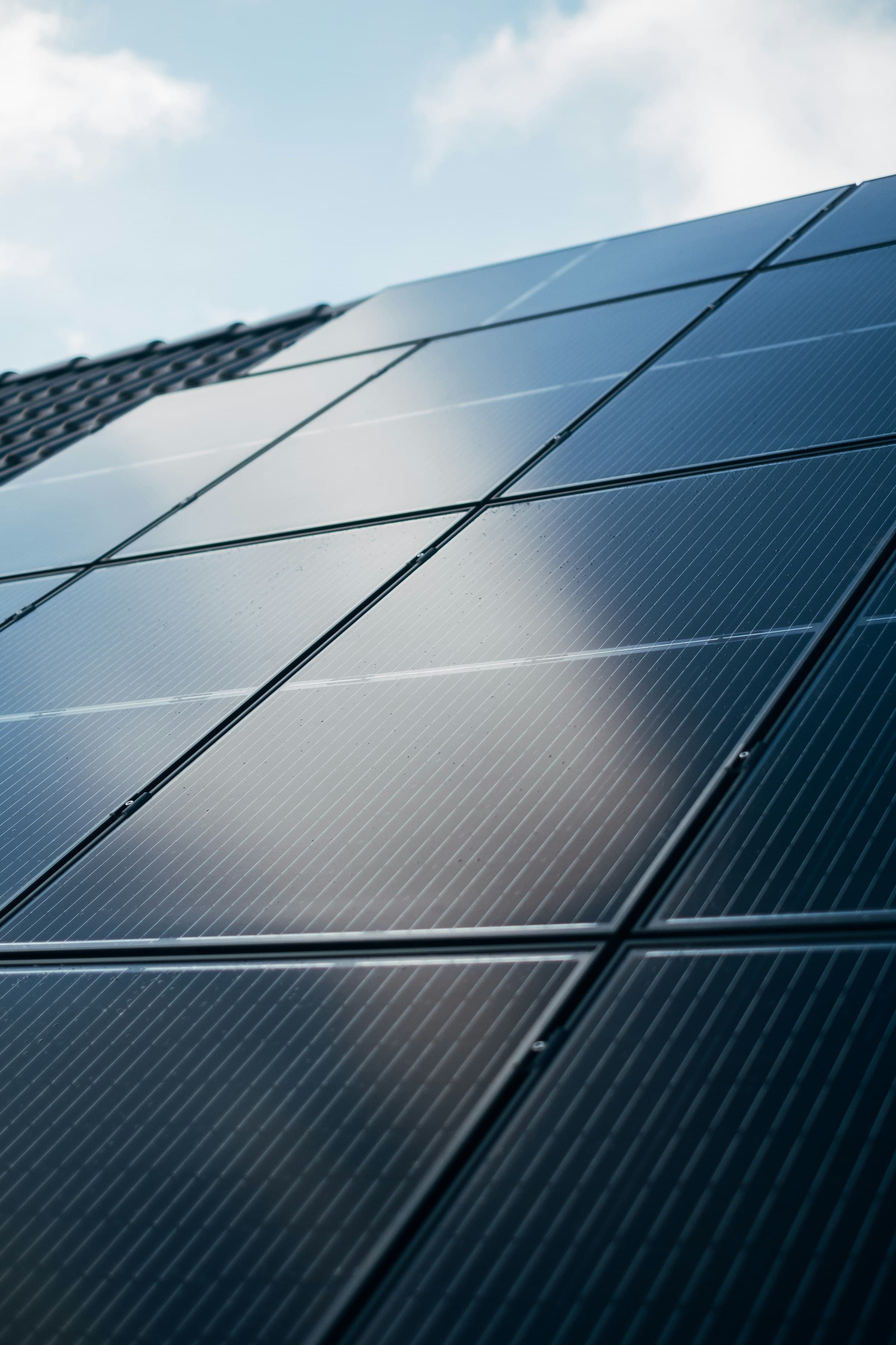 Gros plan sur la grille de cellules d’un panneau photovoltaïque, reflets de ciel nuageux.