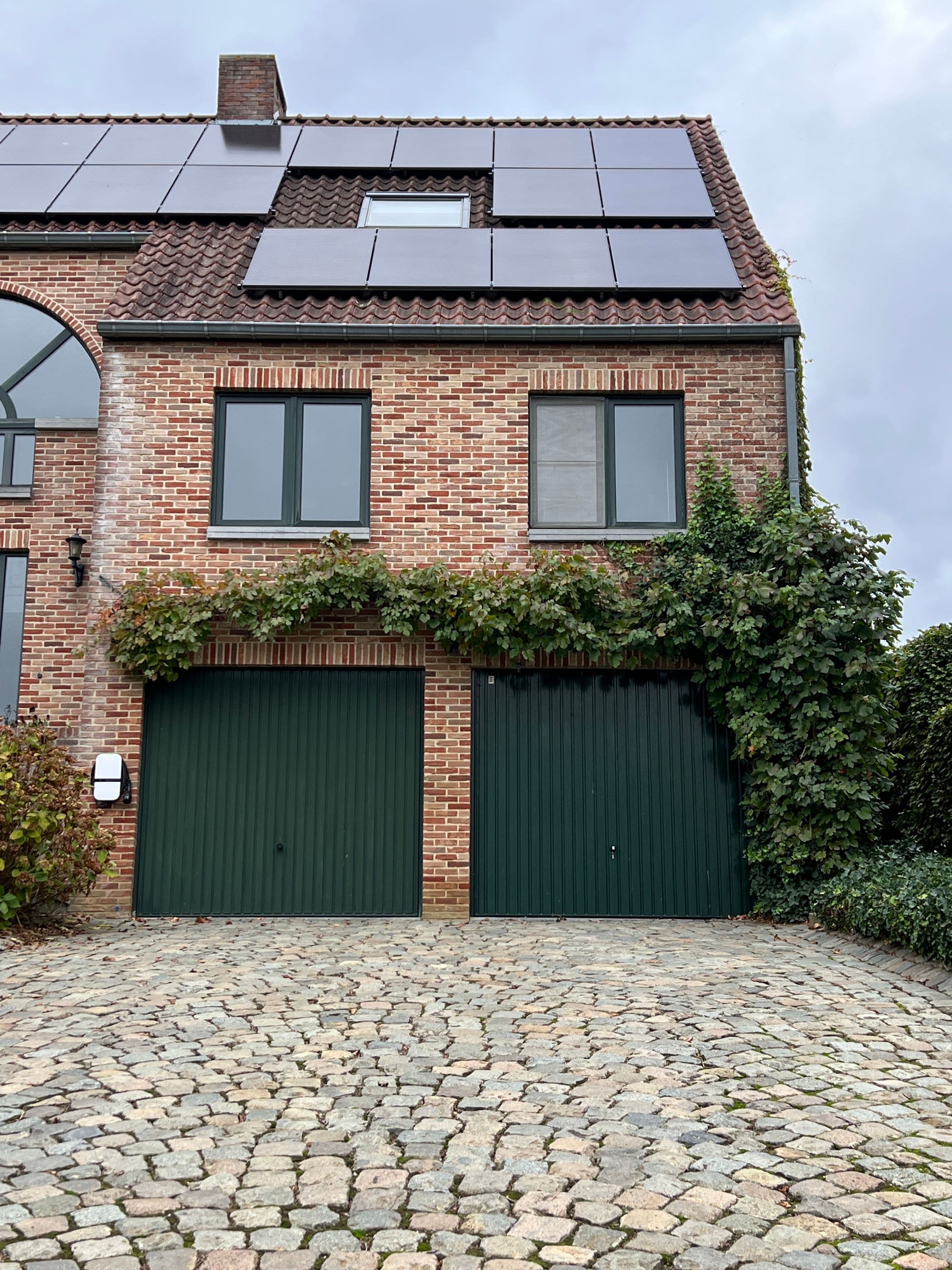 Maison en brique avec toit en tuiles et panneaux solaires noirs bien intégrés, lierre grimpant, allée pavée.