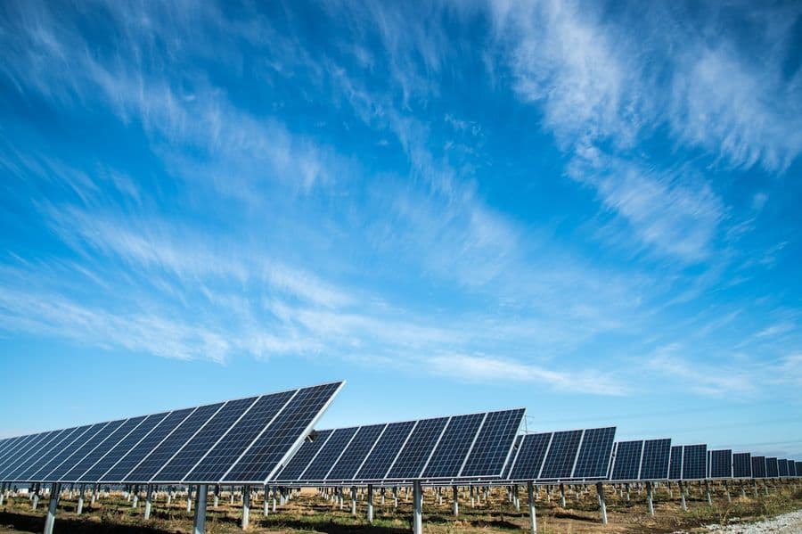Longues rangées de panneaux photovoltaïques au sol sous un vaste ciel bleu strié de nuages.