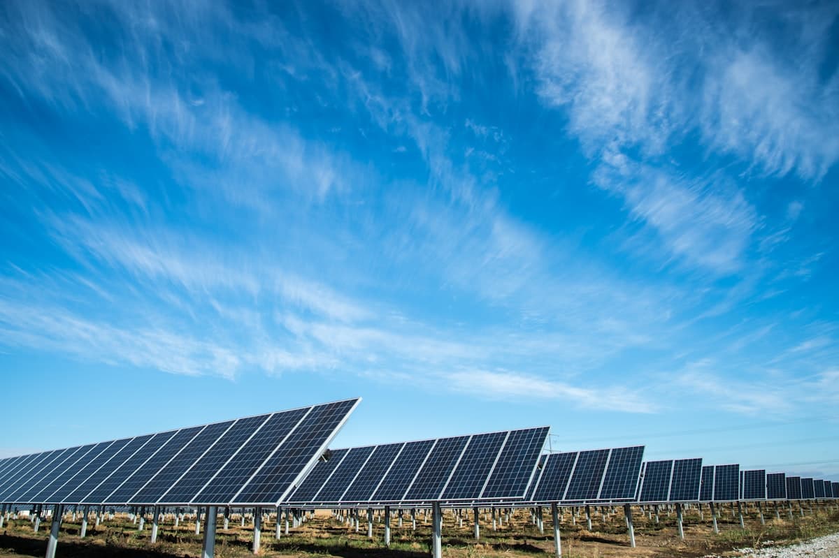 Longues rangées de panneaux photovoltaïques au sol sous un vaste ciel bleu strié de nuages.